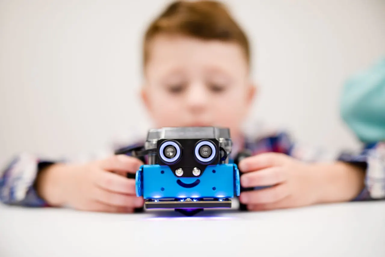 Young child holding a small blue robot with a smiling face and illuminated eyes.