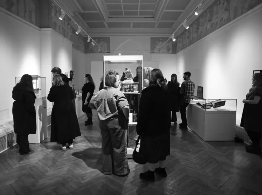 Visitors viewing museum displays and exhibits in a bright gallery space with display cases and white walls.