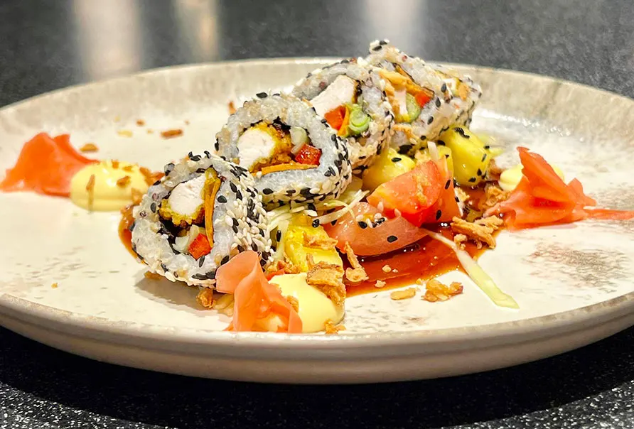 Sushi rolls topped with sesame seeds arranged on a white plate with pickled ginger and yellow garnish.