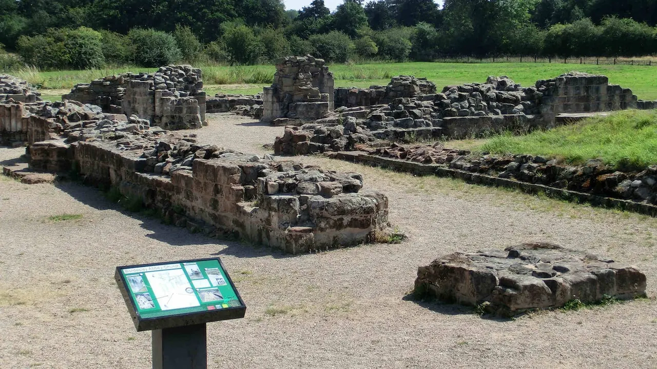 Scattered ancient stone ruins and foundations with an interpretive sign in a grassy pastoral landscape.