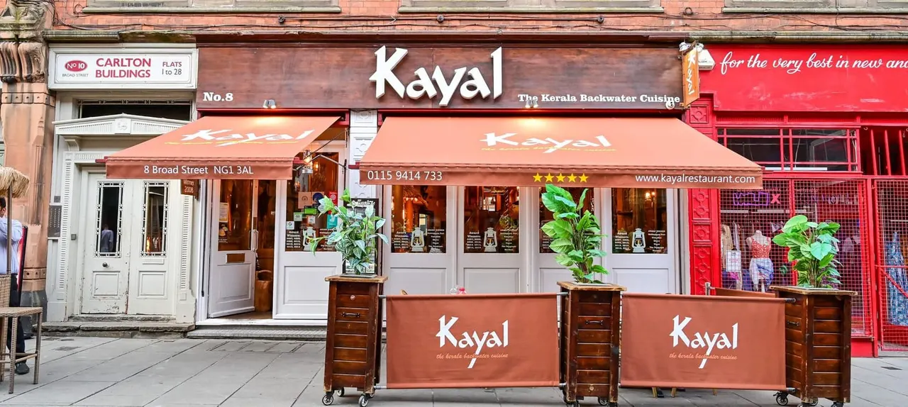 Exterior of Kayal, a Kerala backwater cuisine restaurant on Broad Street, with terracotta awning, potted plants, and wooden barriers outside.