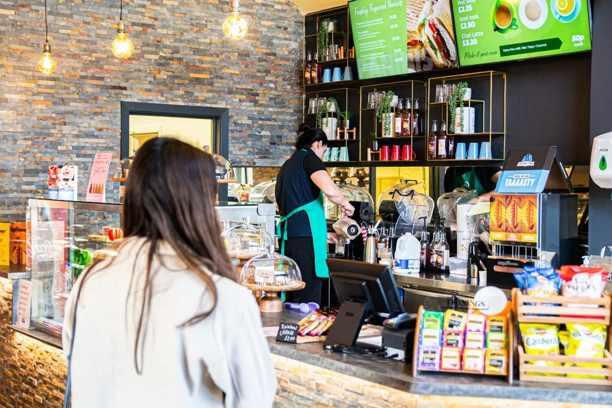 Customer approaches counter at a café with staff member preparing drinks behind the till.