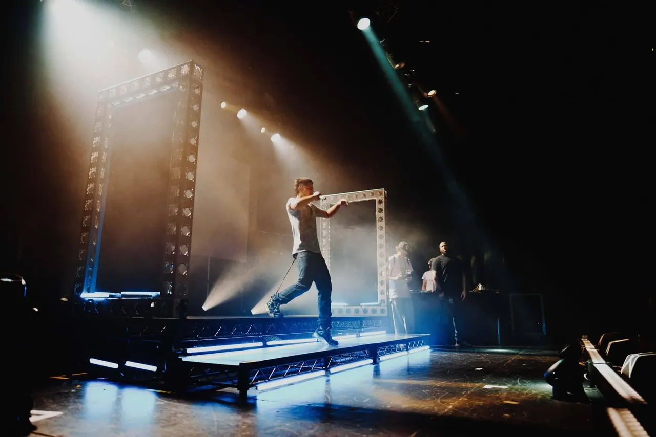 Performer on stage pulling a large metallic frame structure during a concert with dramatic lighting and atmospheric effects.
