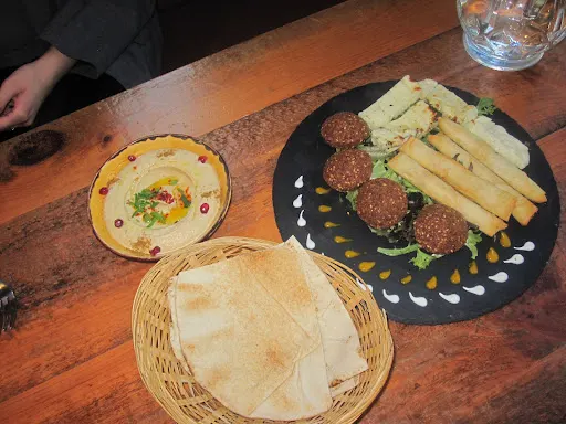 Meatballs with chips and white sauce on black plate, hummus, and warm bread on wooden table.