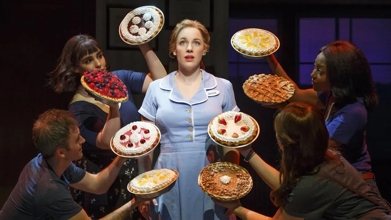 Actors in vintage waitress costumes juggling pies during a theatrical performance scene.