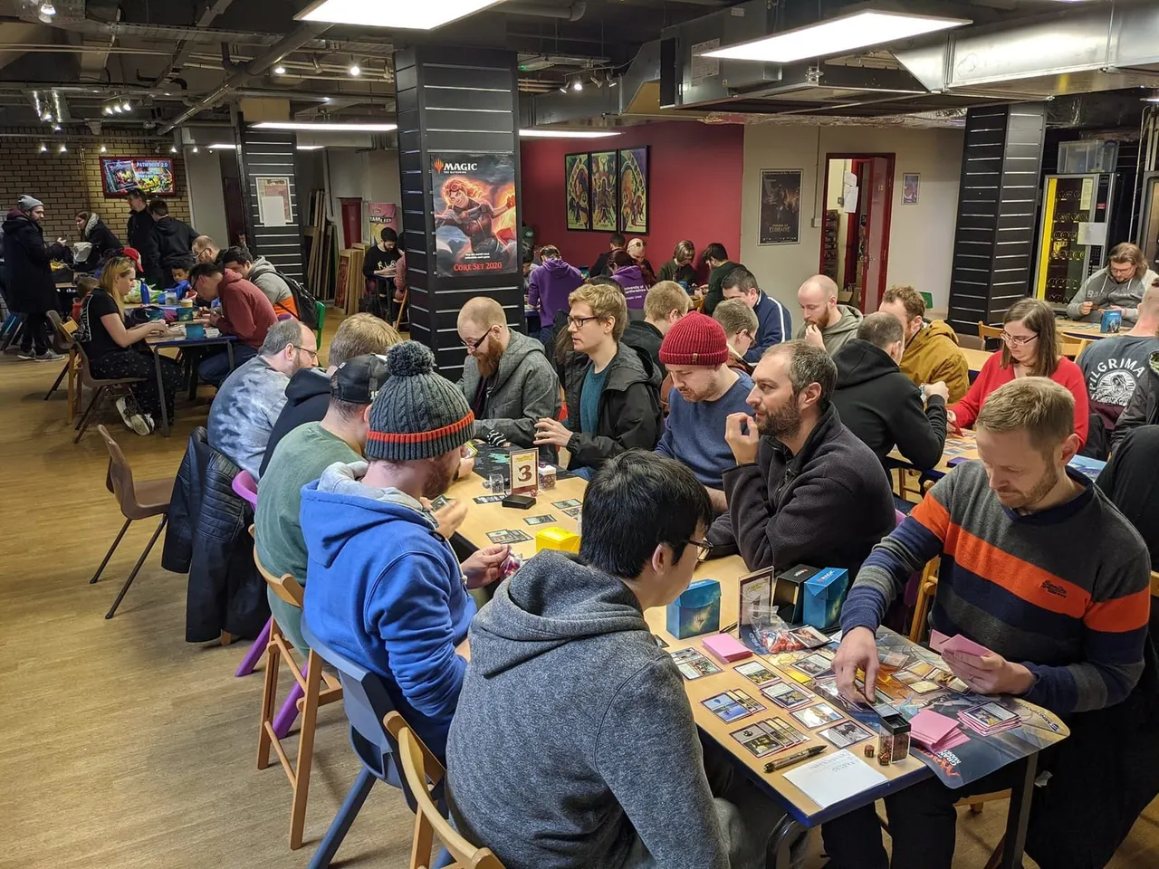 Players seated at tables in a gaming venue playing trading card games during an event.