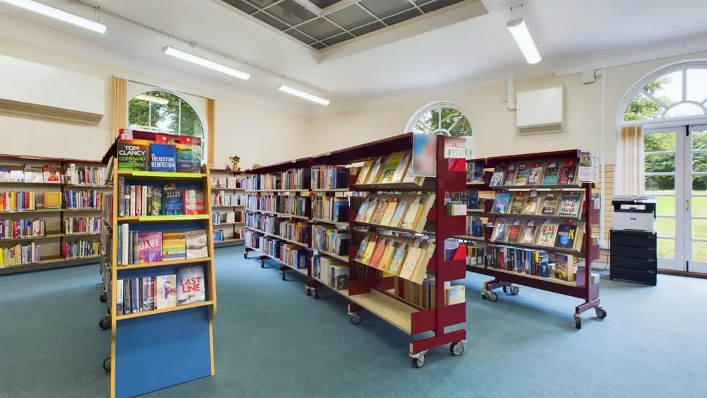 Interior of a library with colourful shelving units displaying books, large windows and natural light throughout the space.