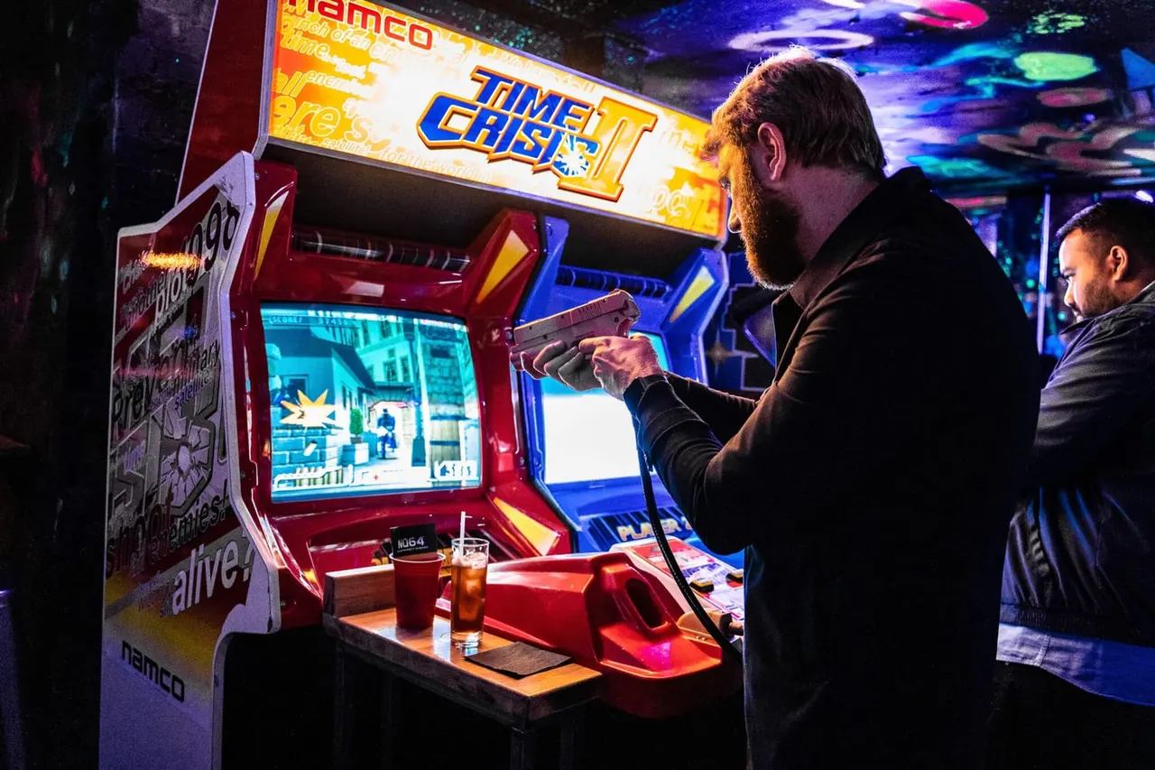 Man playing Time Crisis arcade game at neon-lit gaming venue with other players nearby.