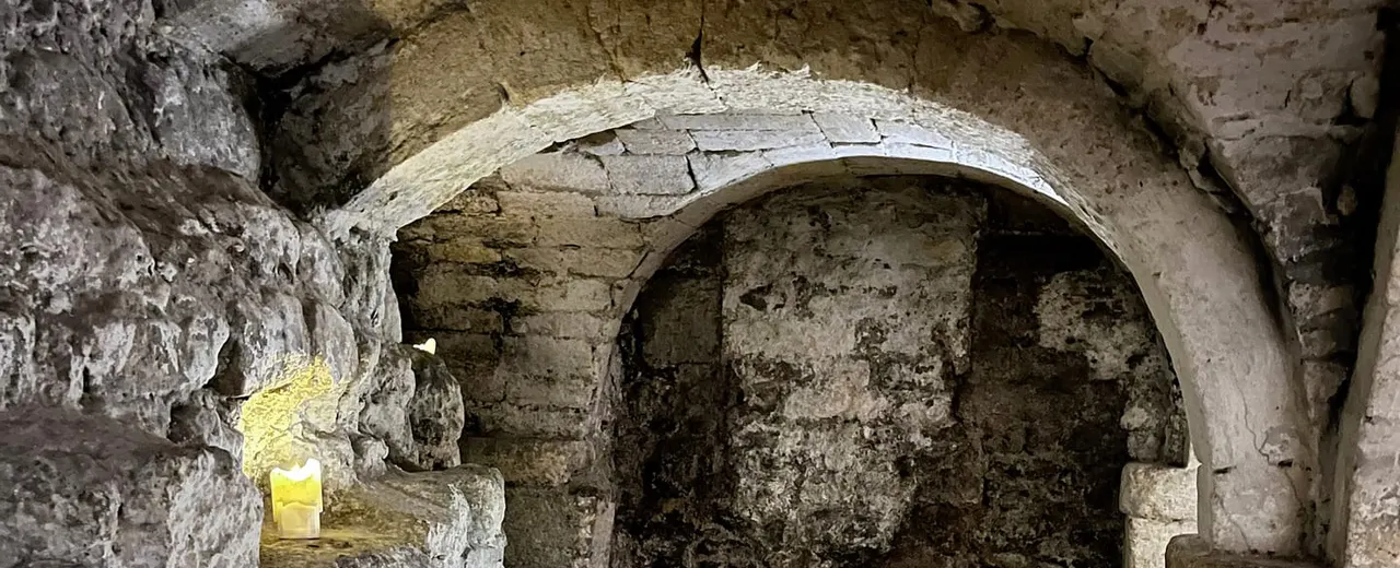 Ancient stone archway and corridor with weathered walls and a lit candle in an underground chamber.