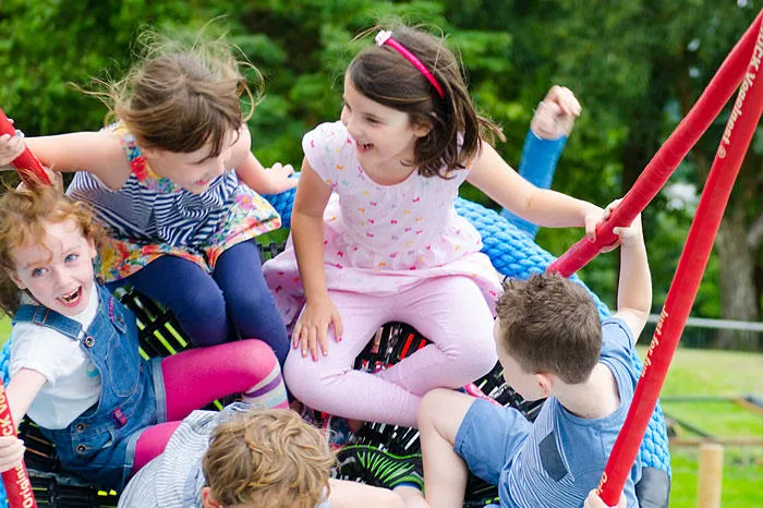Group of young children playing together on red playground equipment outdoors in a garden setting.