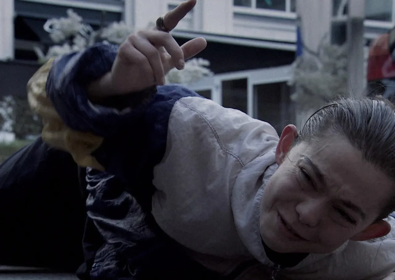 Child pointing upward while lying on ground with buildings in background.