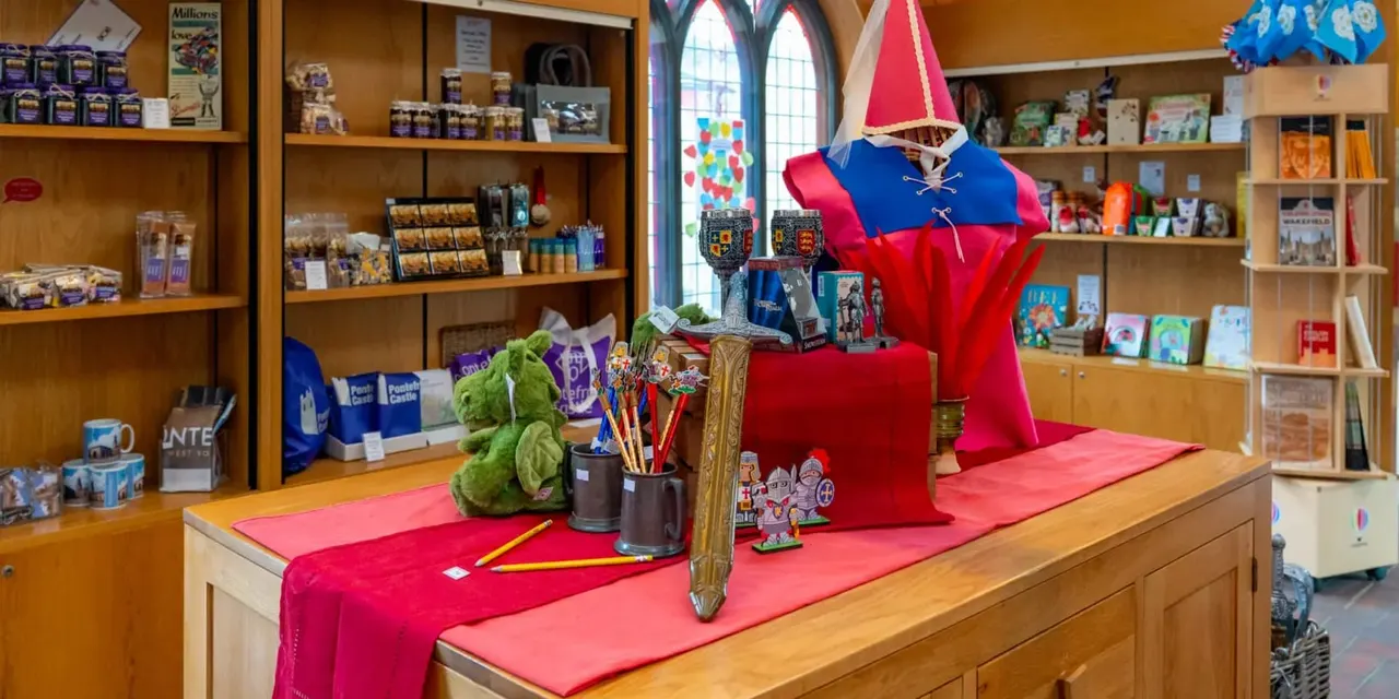 Gift shop interior with wooden shelving stocked with merchandise and a display table decorated in red with a large red and blue fabric castle model.