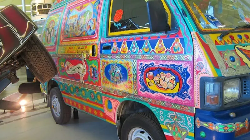 Brightly painted van covered in colourful decorative patterns, displayed indoors at a museum.