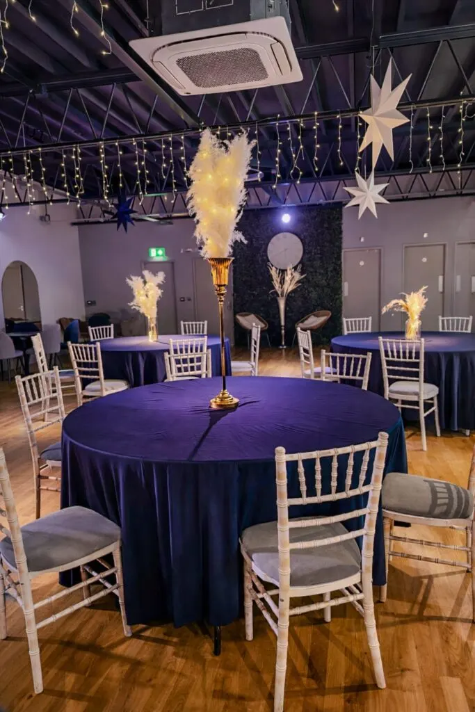 Elegant event space with round tables dressed in deep blue, white chiavari chairs, flame torches, and star decorations overhead.