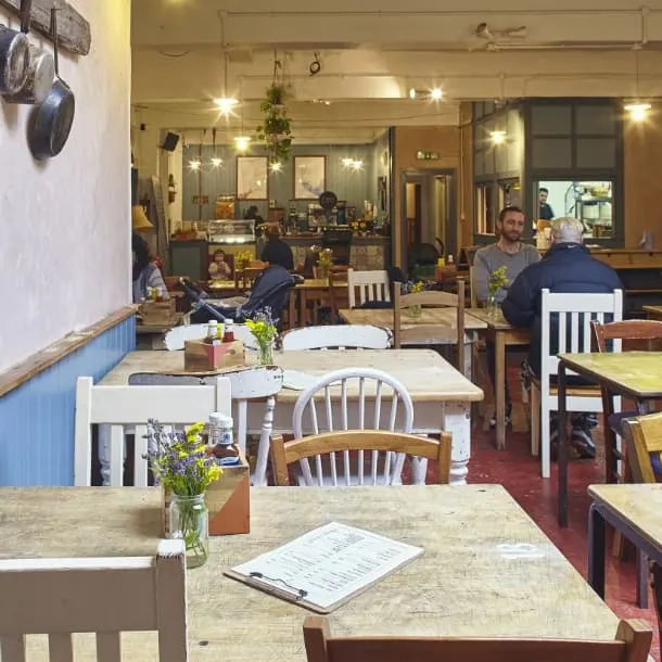 Bright, welcoming café interior with wooden tables, chairs, and fresh flowers, customers seated throughout the space.