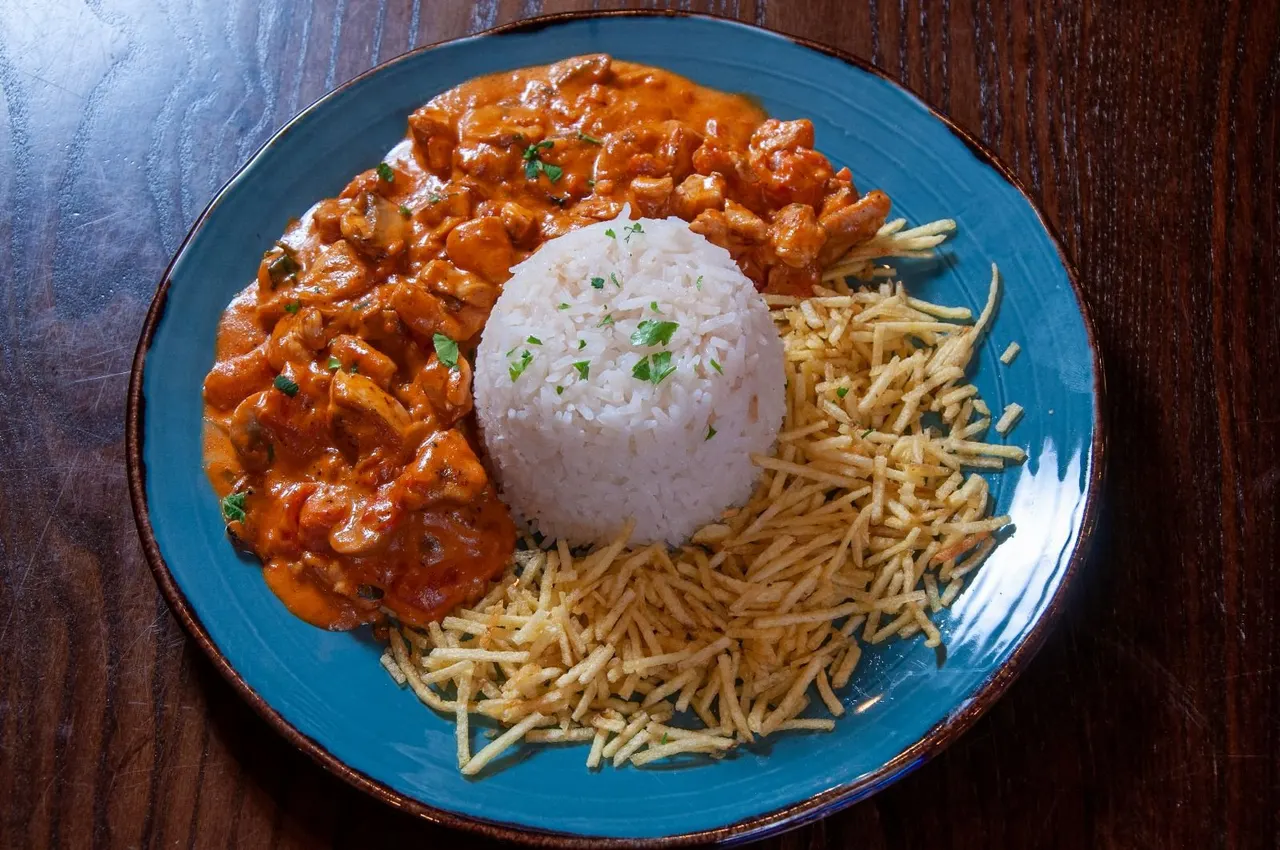 Spicy meat stew served with white rice and crispy fried potatoes on a blue plate.