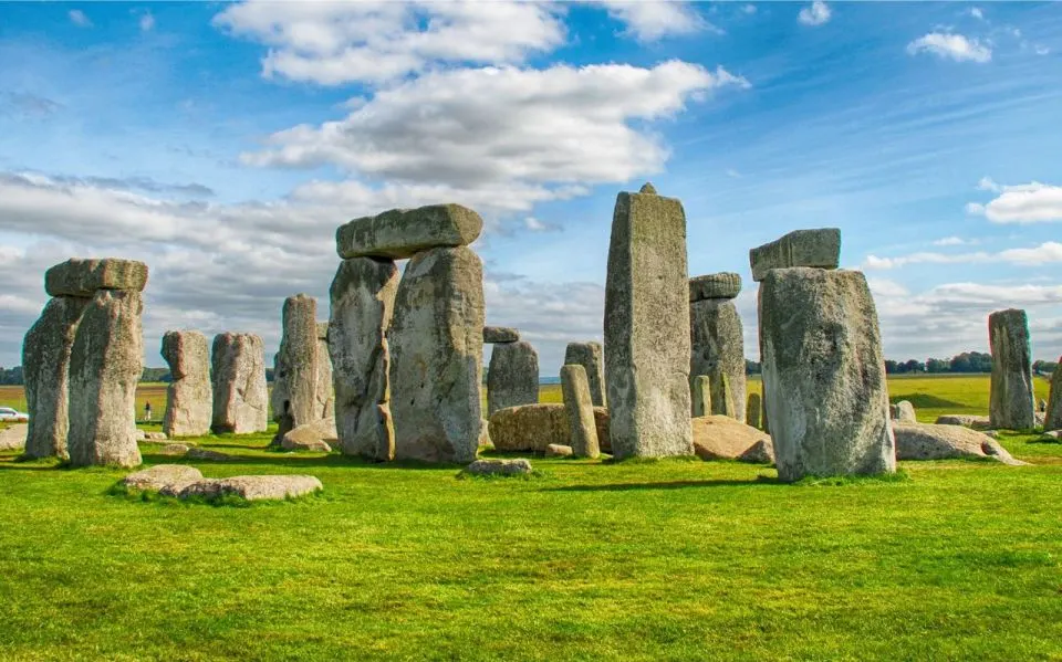 Ancient stone monument with towering monoliths arranged on flat grassland under blue sky with white clouds.