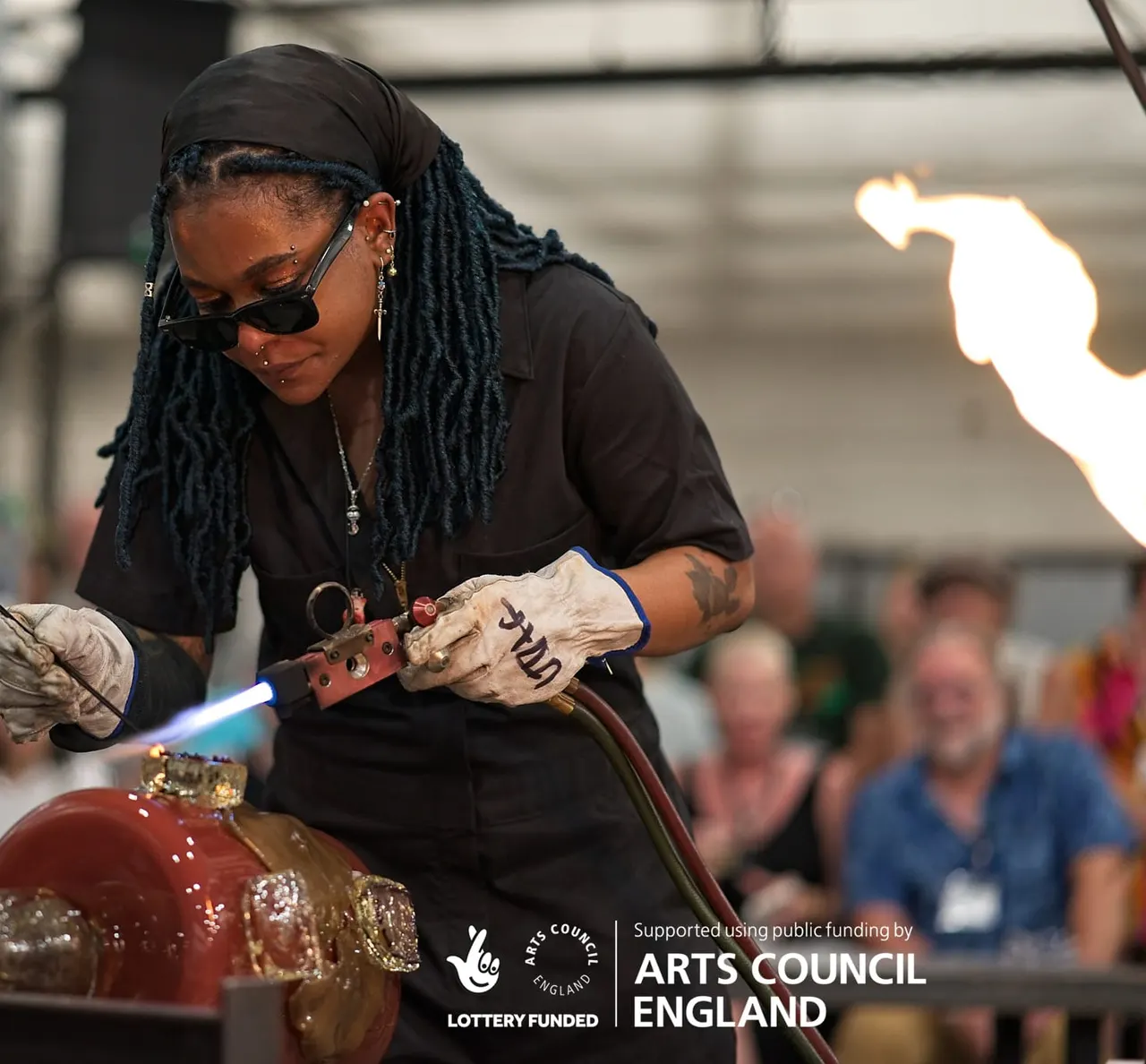 Person using a blowtorch to work with molten glass in a workshop demonstration.