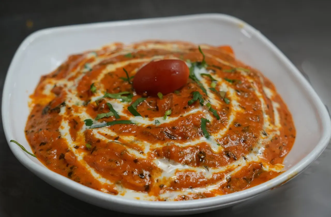 Creamy tomato-based curry dip garnished with fresh herbs and a cherry tomato on a white plate.