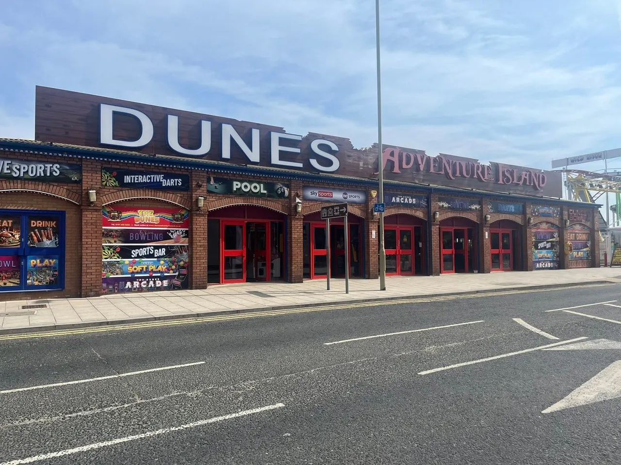 Brick leisure venue with red entrance doors and signage for Dunes pool, bowling, arcade and soft play area on a seafront promenade.