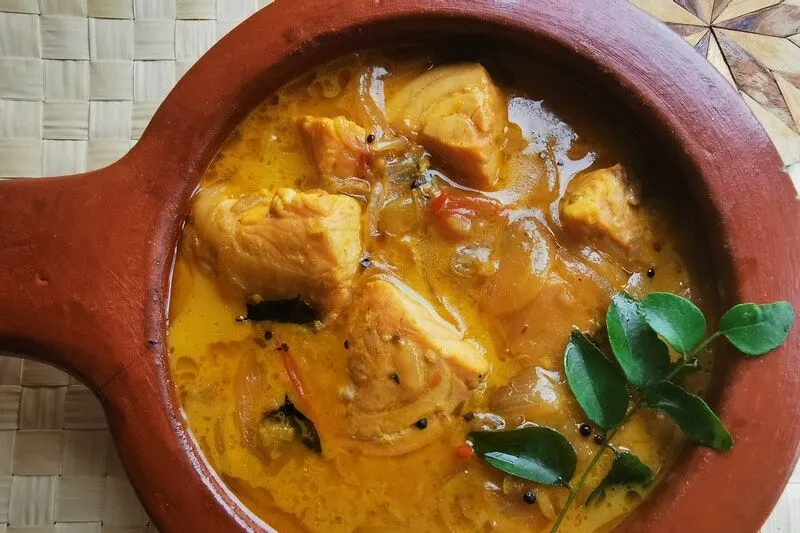 Chunks of chicken in golden curry sauce in a red cooking pot, garnished with fresh herbs.