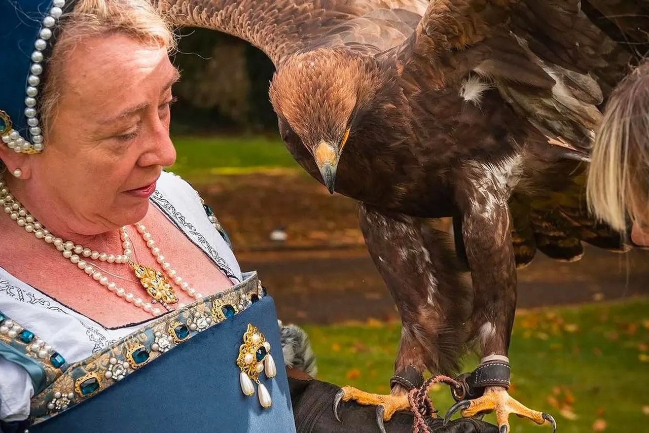Woman in ornate costume with pearl necklace holding a large bird of prey on her gloved hand.