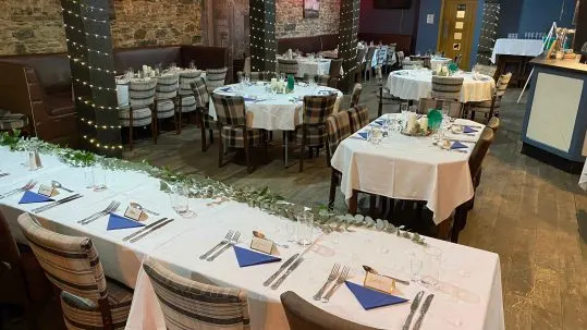 Indoor event space with round tables dressed in white linens and place settings arranged for a formal dinner or banquet.