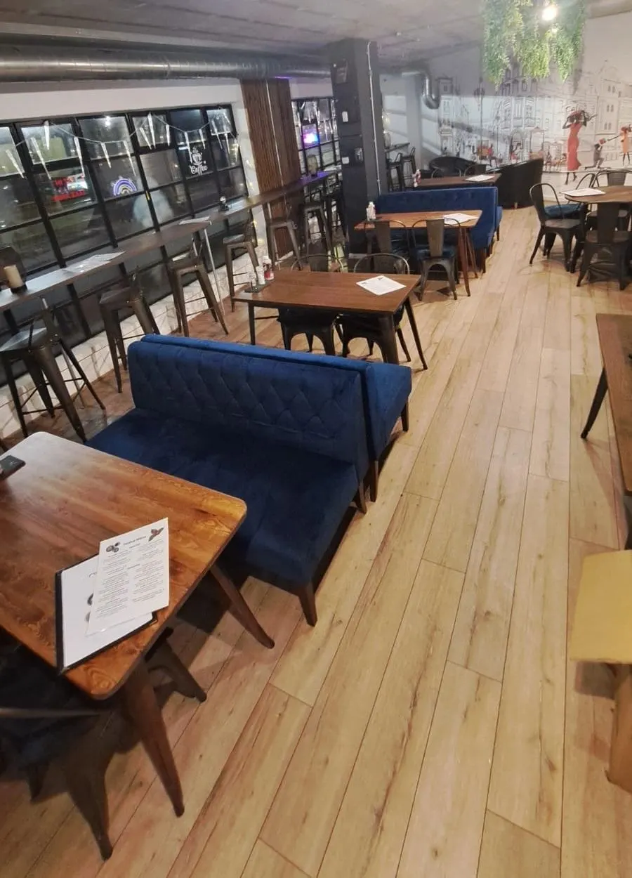 Interior of a café or restaurant with wooden tables, blue upholstered seating, and black chairs on a wooden floor.