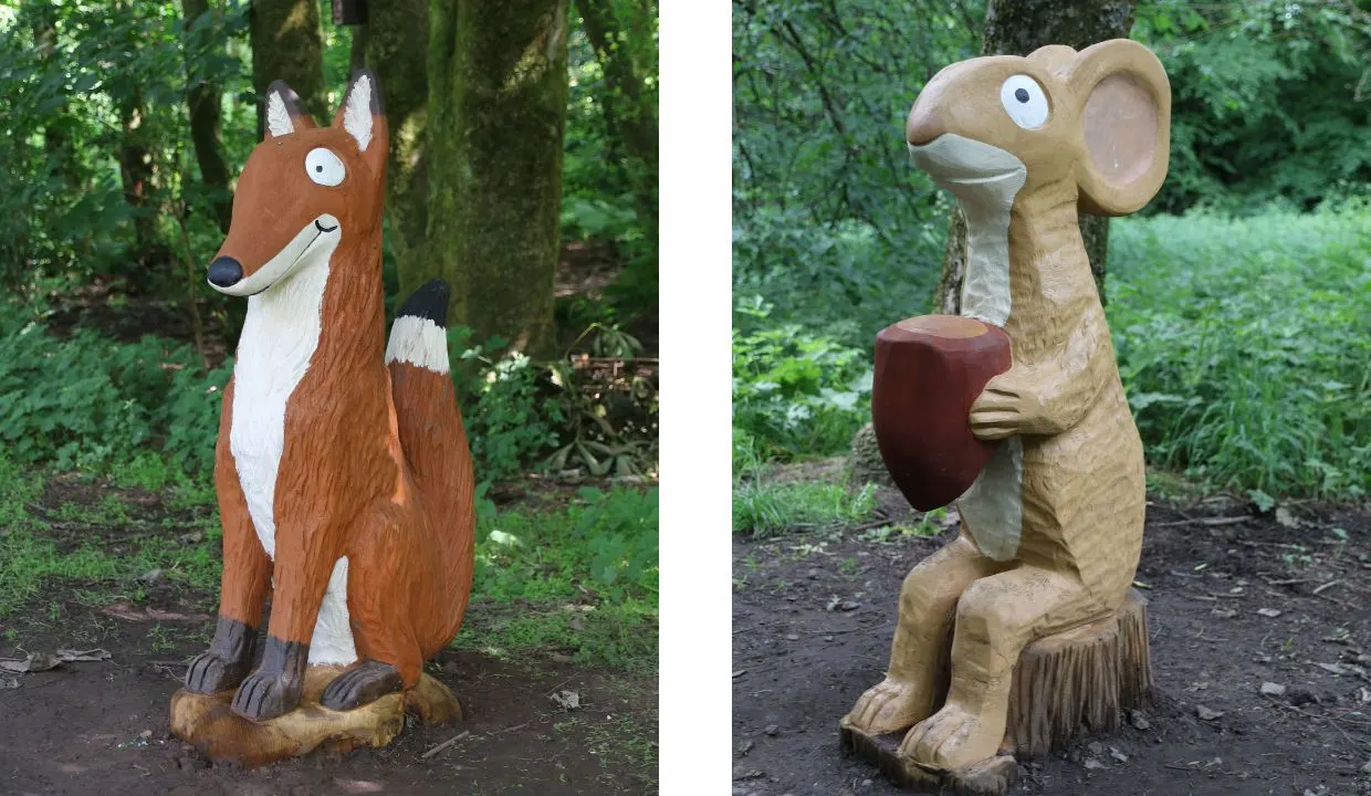 Wooden carved animal sculptures in a woodland setting, including a fox and a meerkat holding a nut.