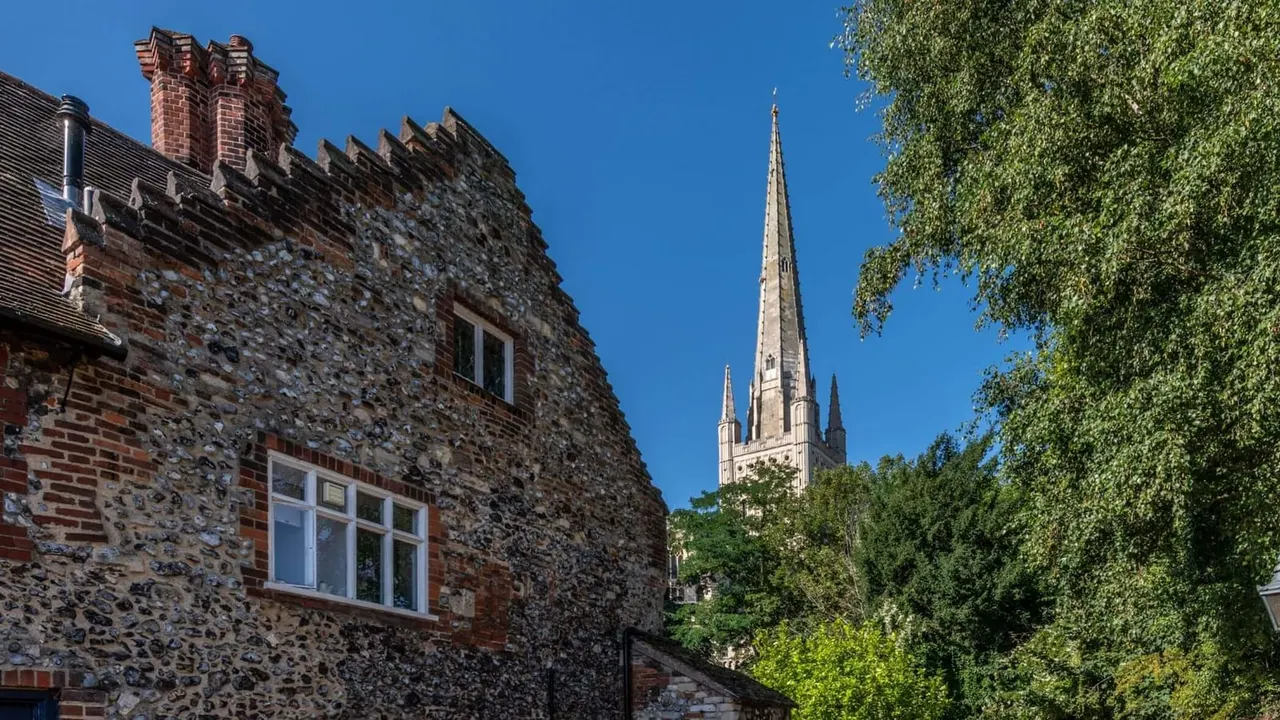 Historic stone cottage with ivy beside a cathedral spire against a clear blue sky.