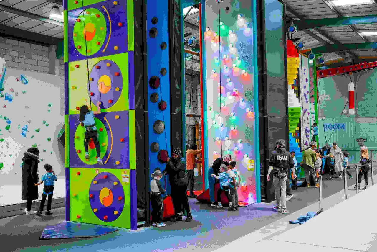 Children and adults climbing coloured indoor climbing walls with handholds in a busy leisure facility.