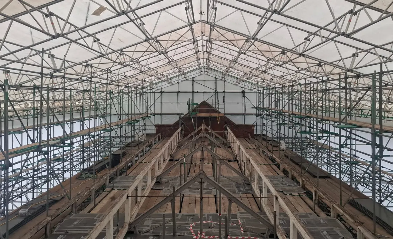 Historic building interior under extensive scaffolding and protective sheeting during renovation work.