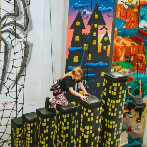 A young child climbs over large black and yellow building-shaped foam blocks in an indoor play area.