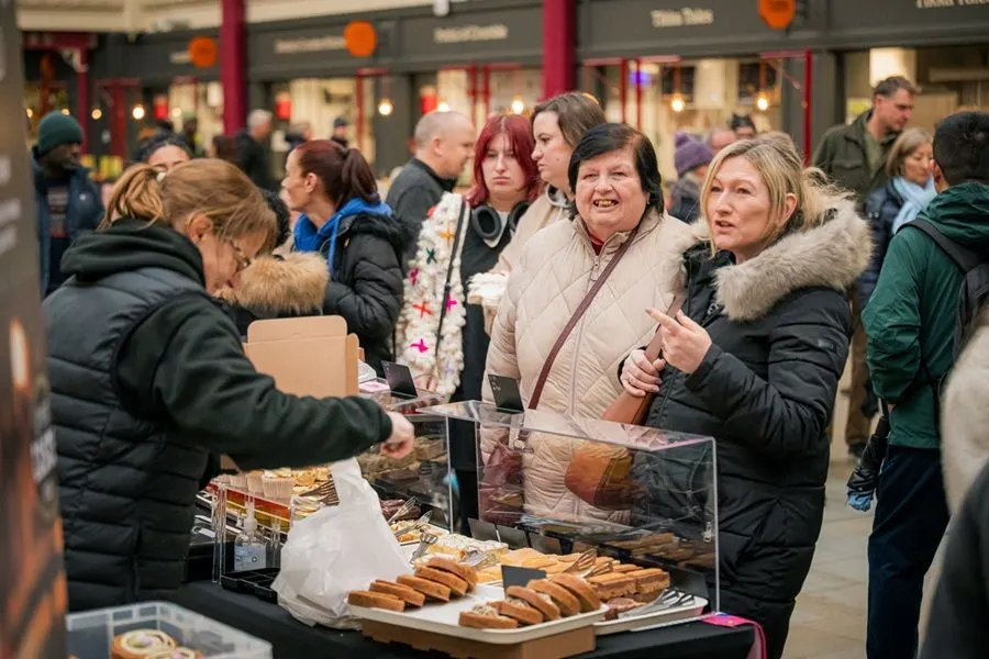 People shopping at an outdoor market stall selling baked goods during a busy festive event.
