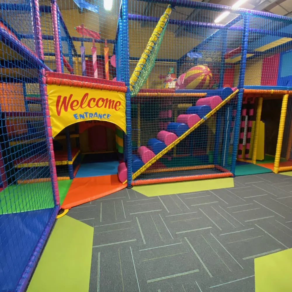 Colourful indoor play structure with bright netting, slides and climbing frames at a children's soft play centre.