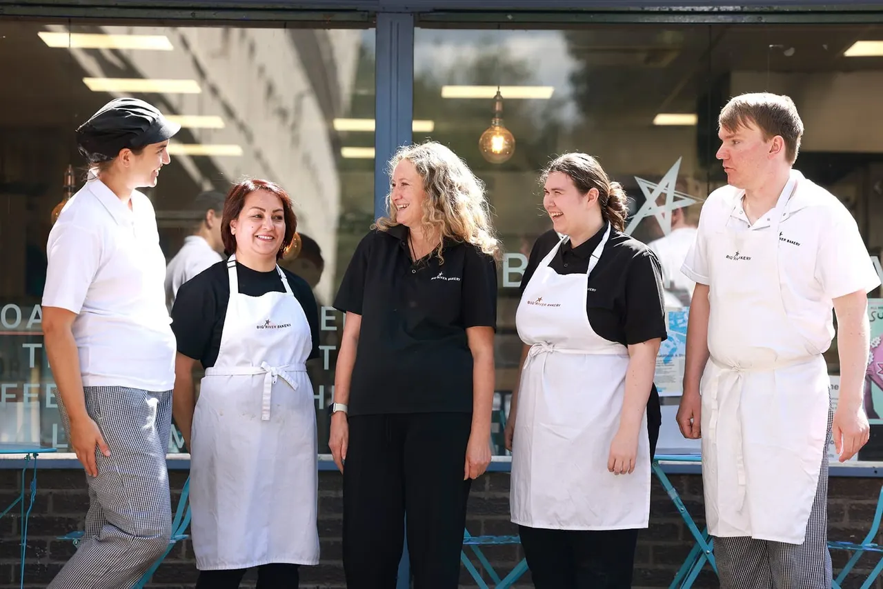 Restaurant staff and owner smiling together outside a bakery storefront.