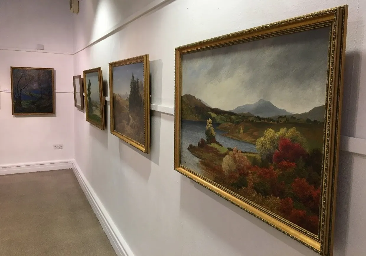 Gallery wall displaying framed landscape paintings of mountains, rivers and countryside scenes in gilded frames.