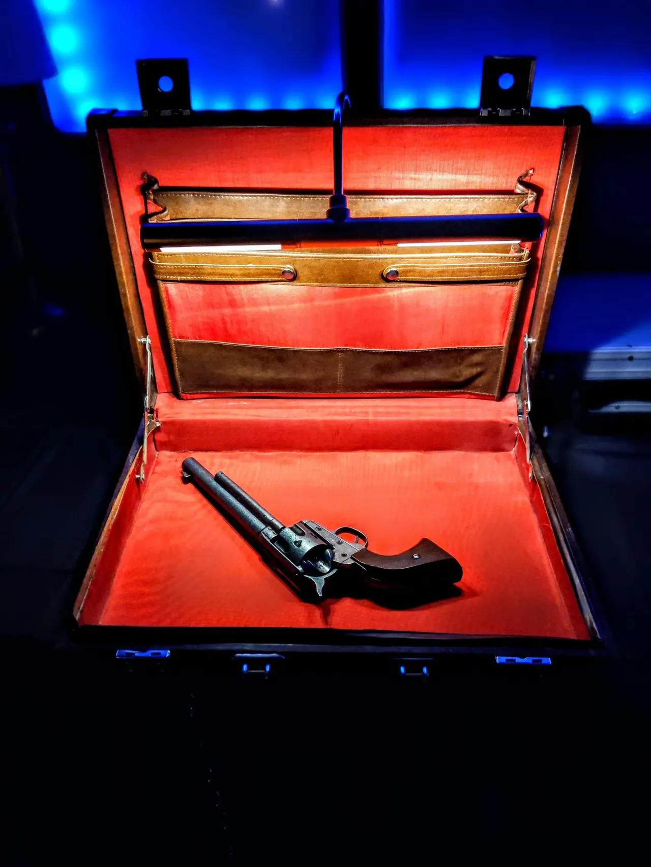 Historical revolver displayed in an open red leather case, museum exhibition lit with blue lighting.