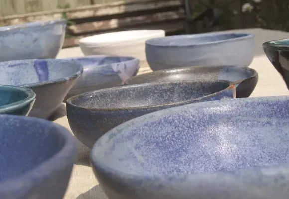 Handmade ceramic bowls in various blue and white glazes displayed in sunlight.