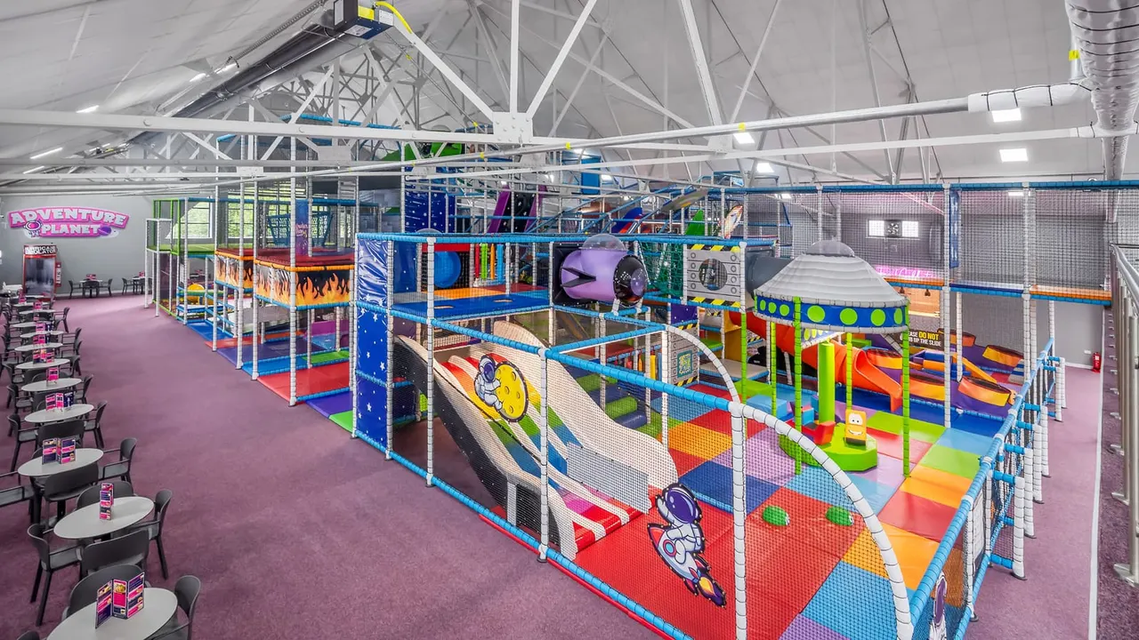 Spacious indoor play centre with colourful multi-level soft play structures, slides and climbing equipment under industrial ceiling.
