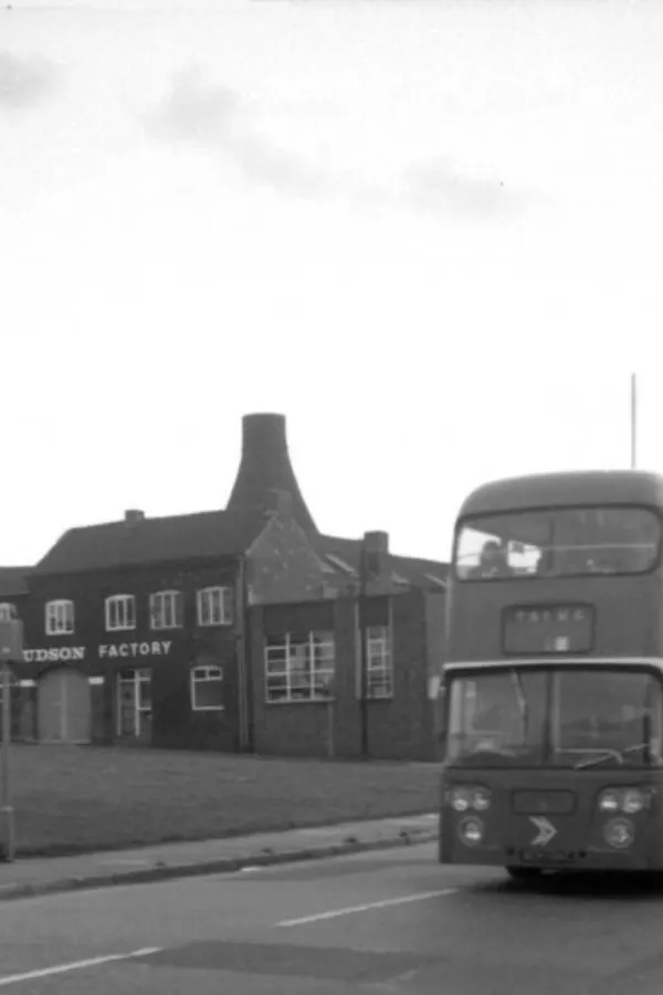 Double-decker bus parked outside a brick factory building with distinctive kiln chimney.