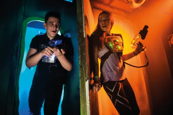 Two young people playing laser tag in neon-lit arenas, holding laser guns.