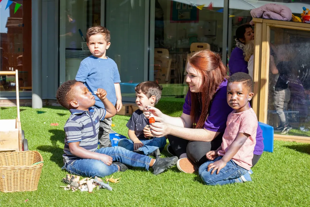 Woman and young children sitting on artificial grass outdoors, engaged in a playful activity together.
