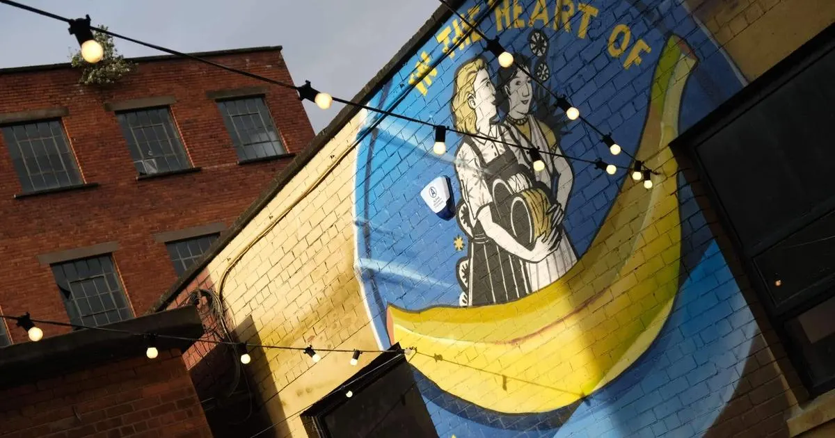 Street art mural on brick buildings depicting two figures in a large yellow banana, with festoon lights strung across.