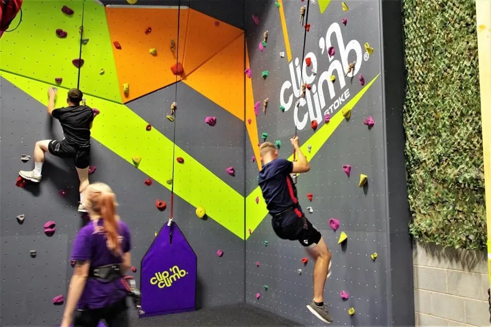 Multiple visitors climbing coloured walls with handholds at an indoor climbing facility.