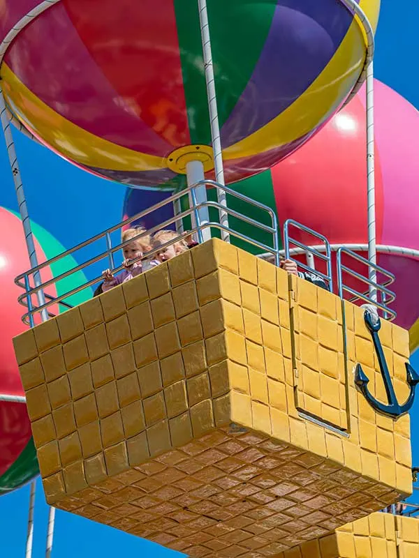 A hot air balloon ride basket suspended beneath a colourful inflated balloon against a blue sky.