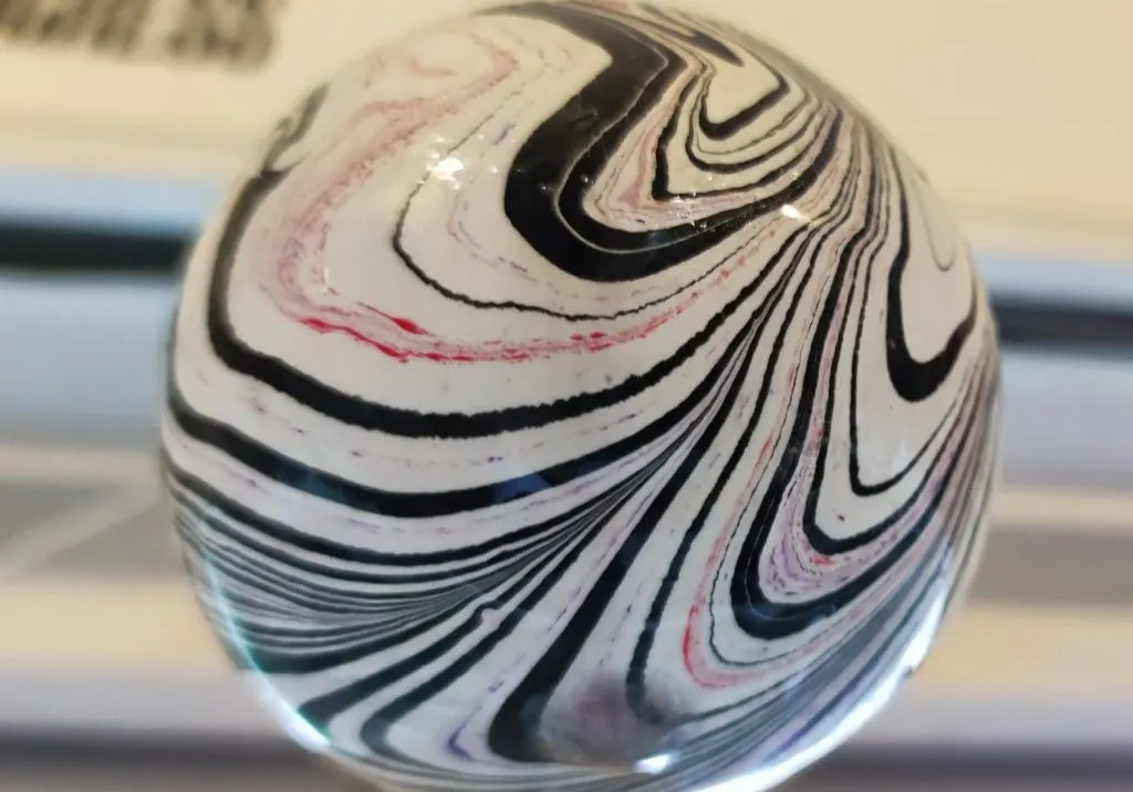 A close-up of a glossy spherical object with swirled patterns in black, white, pink and blue.