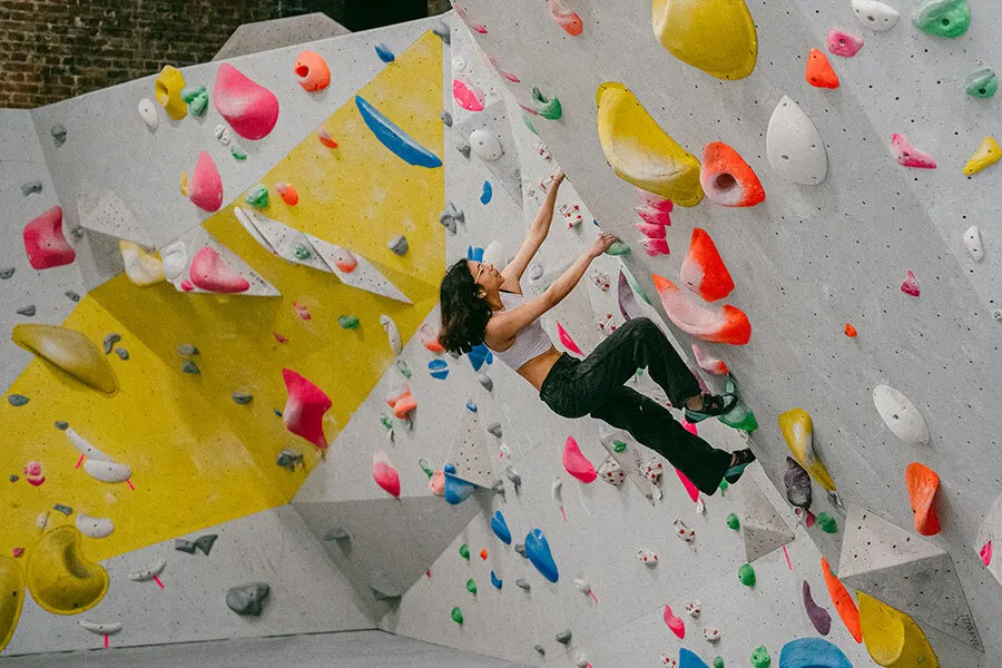 Person climbing an indoor rock wall with colourful holds, viewed from below.