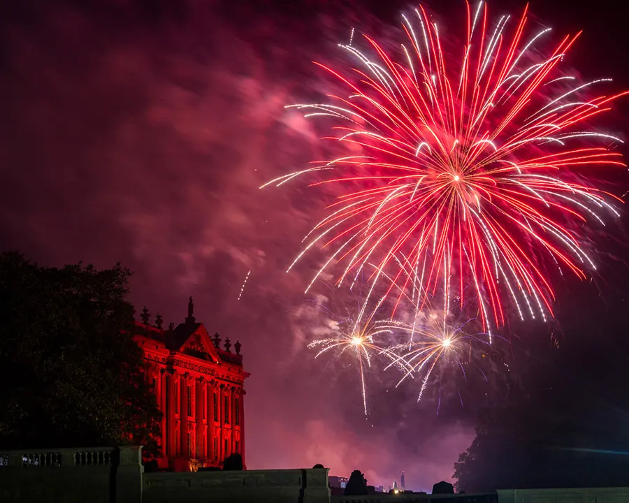Fireworks burst above a historic red-lit mansion at night