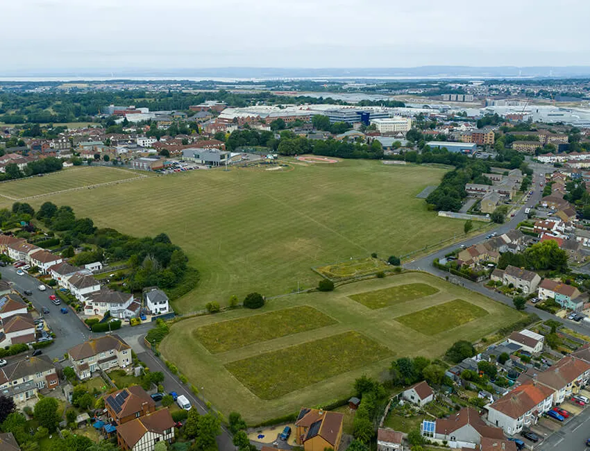 Aerial view of a large sports field surrounded by residential areas, with industrial buildings and countryside visible in the distance.